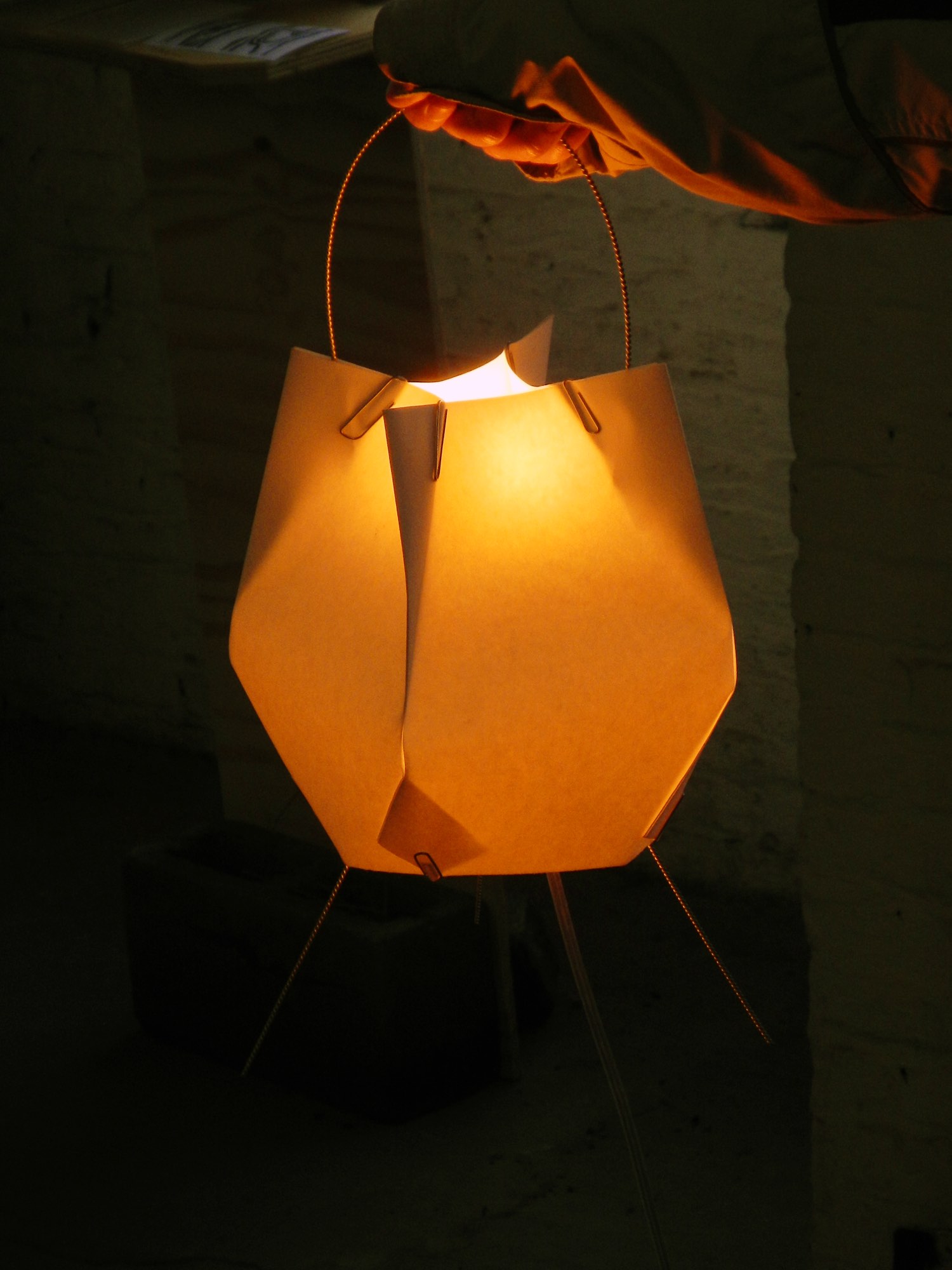 A paper lamp glowing warm orange, held by its wire handle