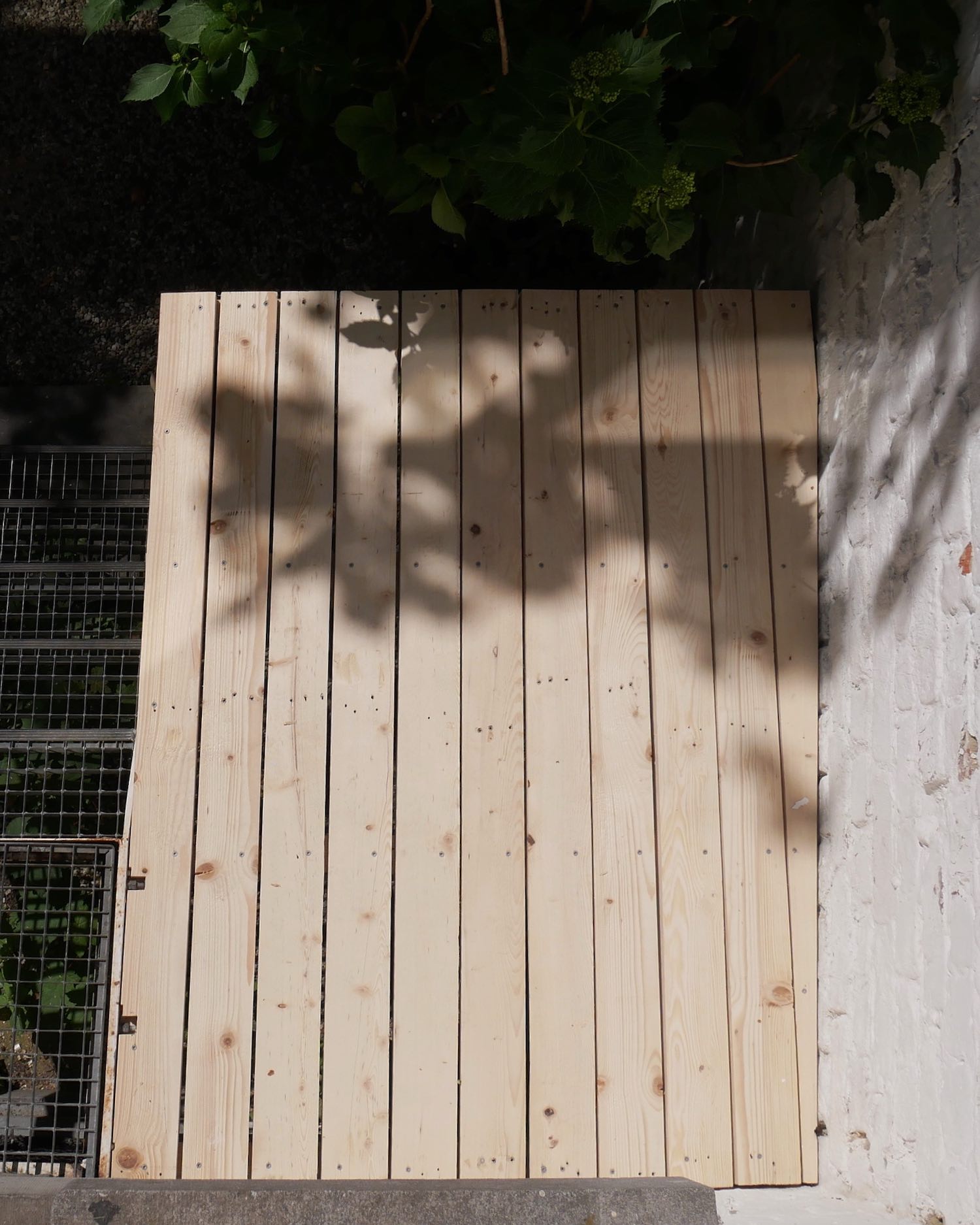 Upper surface of deck: pine boards with the rightmost one trimmed to match angle of brick wall, left side is flush with grating of metal stairs
