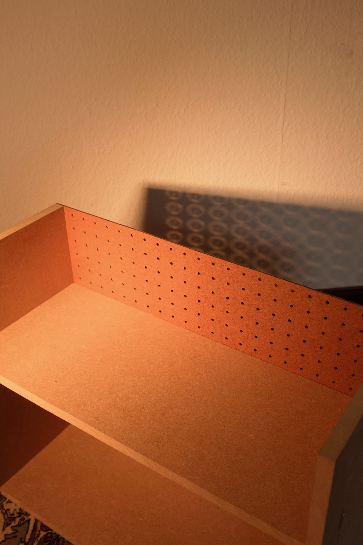 Detail image showing the pegboard backing’s connection to the MDF with the shadow it casts on the wall behind