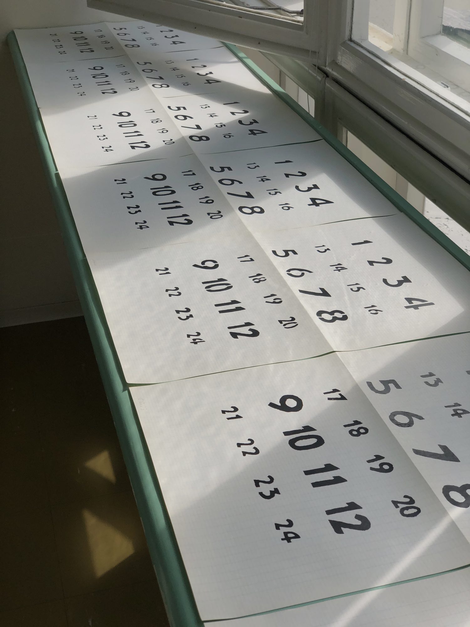 A3 prints of clock numerals on a turquoise desk by a window