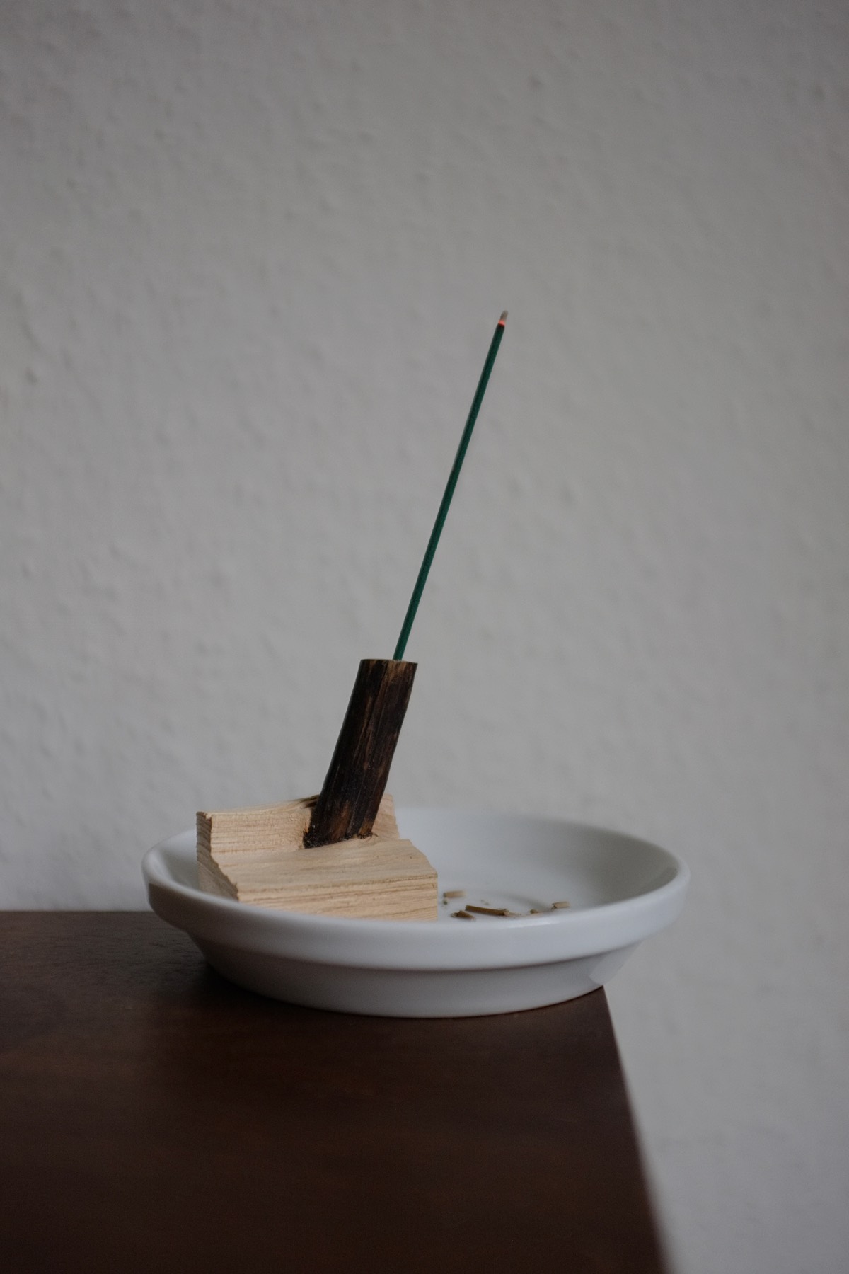 A split piece of pine wood with an internal branch exposed. This branch is cut off and holds a stick of green Japanese-style incense.