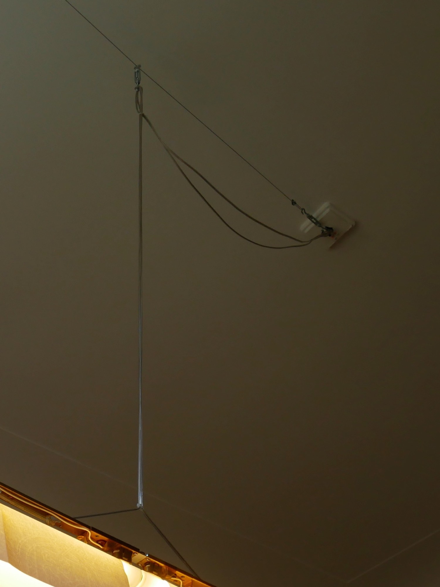 The attachment to the ceiling: the cable is draped loosely and loops around the hook of a turnbuckle